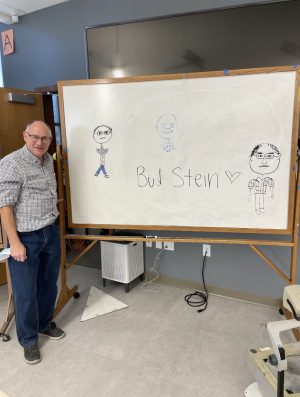 Mr. Stein next to some portraits drawn by his engineering class