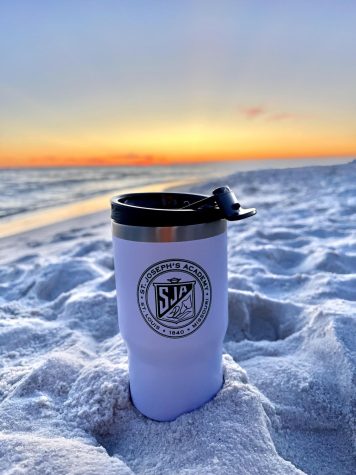 A St. Joe tumbler resting in the sand in front of the sunset at Rosemary Beach. 